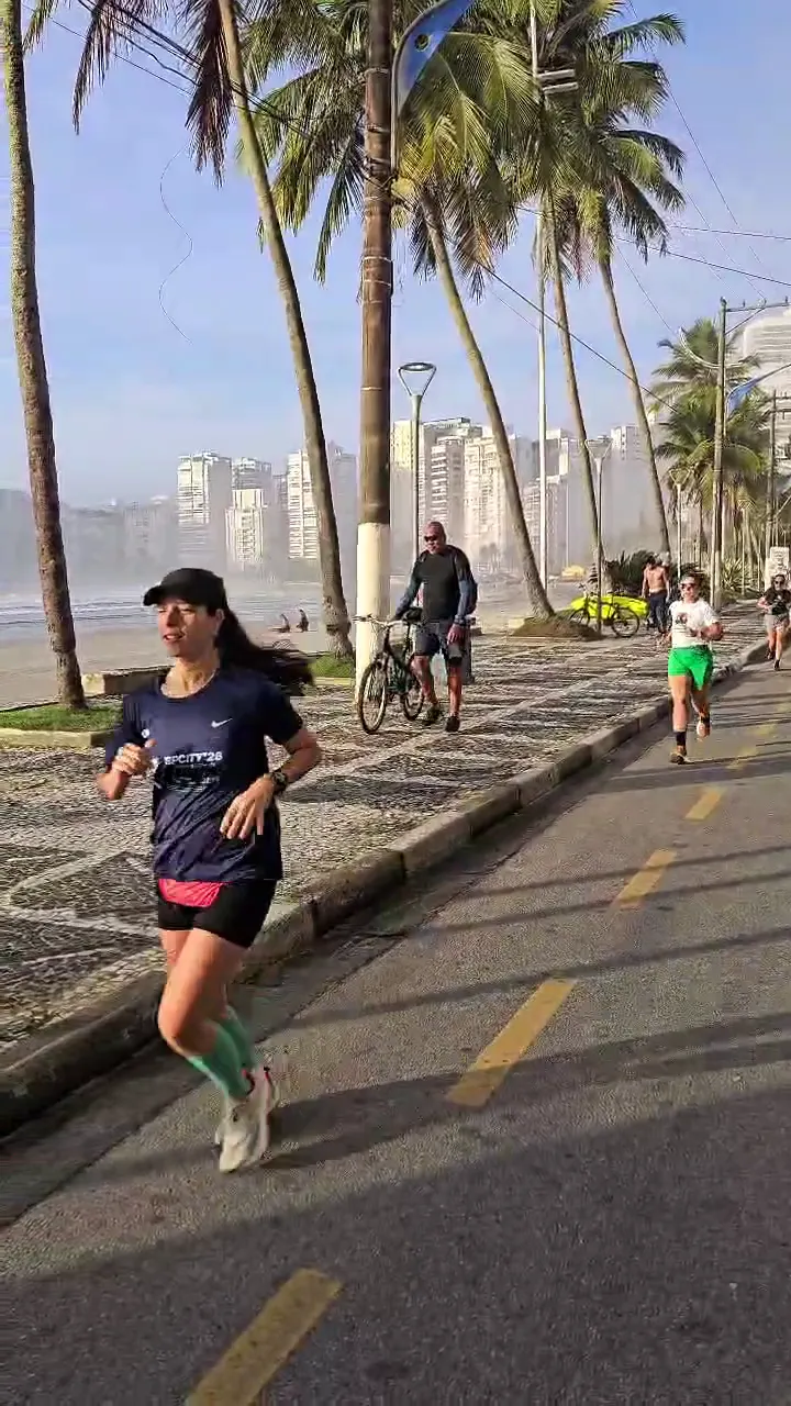 Aluna correndo na ciclovia da orla, entre coqueiros, com outros corredores atrás