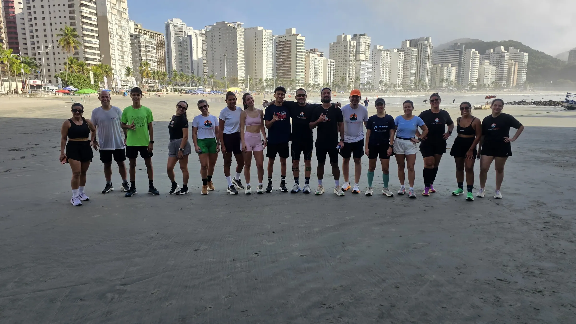 Turma da assessoria do Felipe Corrêa reunida na areia, com os prédios da orla do Guarujá ao fundo